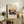 May include: Framed art print featuring a vibrant abstract landscape with blue, yellow, red and green brushstrokes displayed on a rustic wooden sideboard alongside fern plant, stacked books, and ceramic pottery in a neutral-toned living room setting with beige upholstered furniture.