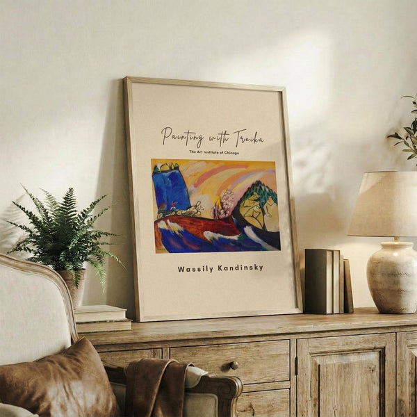 May include: Framed art print featuring a vibrant abstract landscape with blue, yellow, red and green brushstrokes displayed on a rustic wooden sideboard alongside fern plant, stacked books, and ceramic pottery in a neutral-toned living room setting with beige upholstered furniture.