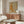 May include: Orange tabby cat artwork hanging above wooden sideboard in modern living room with white curved chair, glass coffee table, and floor lamp. The poster shows a stretching orange cat with floral elements on neutral background in wooden frame.