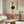 May include: Modern abstract art print featuring geometric circles and semi-circles in beige, olive green, and black tones with concentric line patterns and dotted elements, displayed in thin wooden frame above walnut credenza in minimalist living room with cream upholstered chair, glass coffee table, and contemporary lighting fixtures