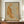 May include: Framed watercolor illustration of an orange tabby cat stretching with arched back, surrounded by delicate botanical elements in soft peach and sage green tones. The artwork is displayed on a wooden sideboard alongside a cream ceramic vase and stacked books against white wainscoting in a warm, neutral-toned room setting.