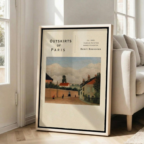 May include: Framed art print leaning against white wall next to beige upholstered chair in bright room with large windows. Print shows pastoral village scene with orange-roofed houses, small figures walking on dirt path, green trees and cloudy sky. Text reads "Outskirts of Paris" and "Henri Rousseau" with museum-style formatting on cream background. Light wood frame with black mat border.