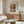 May include: Framed art poster displayed above wooden sideboard in modern living room with white curved chair and glass coffee table. Poster features colorful still life with flowers in striped vase and oranges in Matisse's distinctive cut-out style, with blue, pink, and coral background sections. Room has neutral walls, natural lighting, and contemporary furniture with warm wood tones.