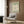 May include: Framed Matisse-inspired poster with sage green background and cream colored abstract flower cutout design, displayed on wood paneled wall above beige upholstered armchair with geometric patterned pillow, brass floor lamp and side table with open book nearby