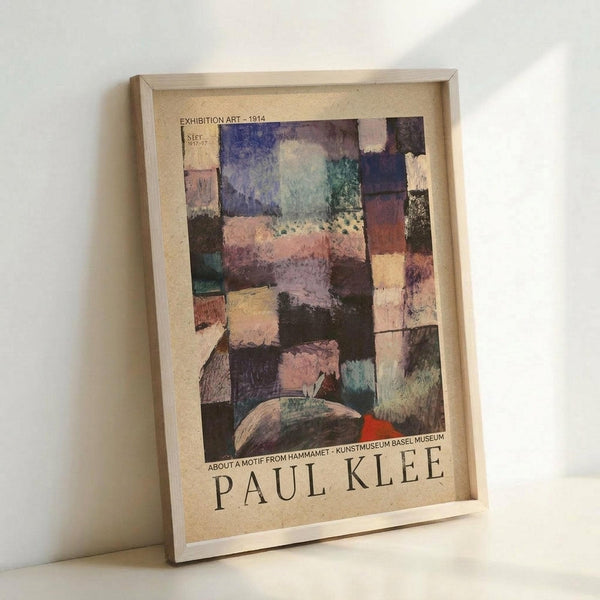 May include: Framed exhibition poster featuring Paul Klee's abstract artwork with colorful geometric squares and rectangles in blues, purples, pinks, and earth tones. The vintage-style poster shows museum text and sits in a light wooden frame leaning against a white wall on a white surface.