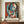 May include: Framed Picasso-style cubist poster featuring abstract woman with geometric blue and white face, red lips, black hair, displayed on wooden sideboard next to white ceramic vase and books in elegant room with white paneled walls