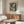 May include: Framed Pablo Picasso exhibition poster featuring colorful cubist portrait of a woman with geometric shapes in blues, reds, and warm tones, displayed above a mid-century modern walnut credenza with white marble top. Room scene shows cream upholstered swivel chair, glass oval coffee table, brass floor lamp, and white sculptural vase on polished floors with soft natural lighting.