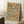 May include: Framed vintage-style poster with botanical illustrations in earth tones - green, rust, blue, and cream colors featuring tropical leaves, flowers, and sun motifs with "Nature's Essence" text and "Hand Printed on Recycled Paper - Est. 1975" at bottom. Shown leaning against white wall in cozy room setting with coffee cup on wooden surface and cream knit throw blanket on white textured rug.