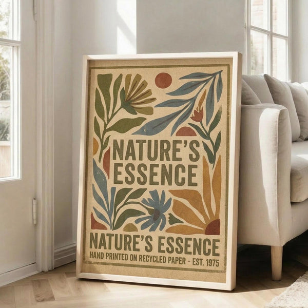 May include: Framed vintage-style botanical poster with earthy tones featuring stylized leaves, plants, and circular sun motifs in greens, oranges, and blues on cream background. White frame leans against wall beside beige sofa in bright room with white walls and large windows.