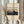 May include: Hands holding a framed poster print showing Mount Fuji with pink sunset sky, dark silhouetted hills and traditional Japanese houses below. Light wood frame on cream mat, held against white curtained window with dried pampas grass visible to left side.