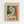 May include: Framed art print displayed on white wall featuring cubist-style portrait of woman with tilted head in geometric shapes. Artwork shows green, orange, yellow, and cream color palette with angular facial features and fragmented forms. Light wood frame surrounds cream-colored mat with "PICASSO" text at top and small French description at bottom.