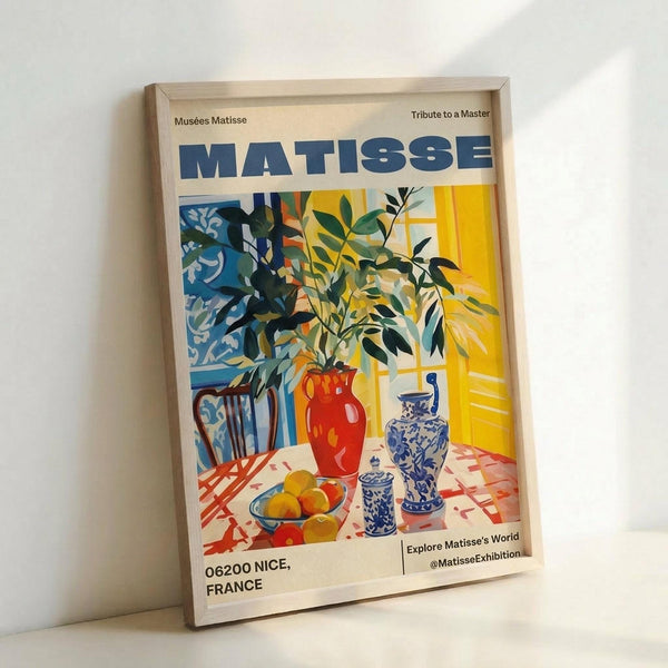 Framed poster featuring a vibrant Matisse-style still life with red vase filled with green foliage, blue and white decorative pottery, yellow fruit on checkered tablecloth, and ornate chair against sunny yellow interior. Bold colors include blues, reds, yellows, and greens in characteristic cut-out aesthetic. Light wood frame displayed against white wall, leaning on surface with soft shadows.
