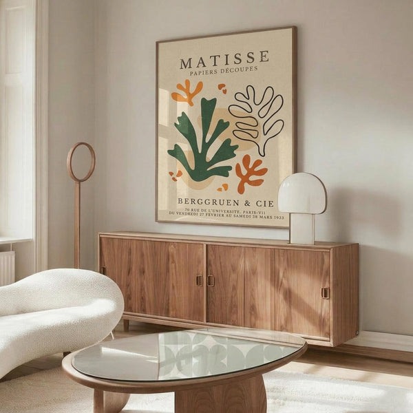 May include: Matisse-inspired botanical art print with orange and green abstract leaf shapes on cream background, displayed above walnut credenza in modern living room with white curved chair, glass coffee table, and soft natural lighting