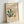 May include: Framed vintage-style art print featuring Matisse paper cutout designs in green, orange, and beige organic shapes resembling coral or seaweed forms. Cream background with "Berggruen & Cie" gallery text and Paris exhibition details. Light wooden frame leaning against white wall on light surface.