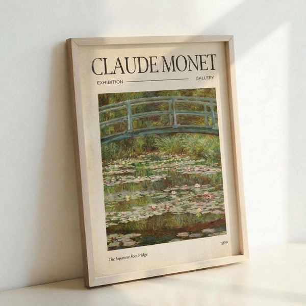 May include: Framed exhibition poster featuring Claude Monet's Japanese Footbridge painting from 1899, showing a curved blue-green bridge over a pond with water lilies and lush vegetation. The poster has clean typography with "CLAUDE MONET EXHIBITION GALLERY" at the top and artwork details below. Light wooden frame sits against white wall, casting subtle shadows.