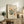 May include: Framed Matisse-inspired poster with abstract botanical cutout shapes in green, orange and beige on cream background, displayed on rustic wooden sideboard alongside fern plant, books, ceramic vase and brown leather chair in neutral-toned living room setting