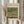 May include: Hands holding a framed exhibition poster featuring Monet's Japanese Footbridge painting from 1899, showing a green arched bridge over a water lily pond. The cream-colored poster is in a light wood frame, held alongside dried pampas grass stems against flowing white curtains in soft natural lighting.