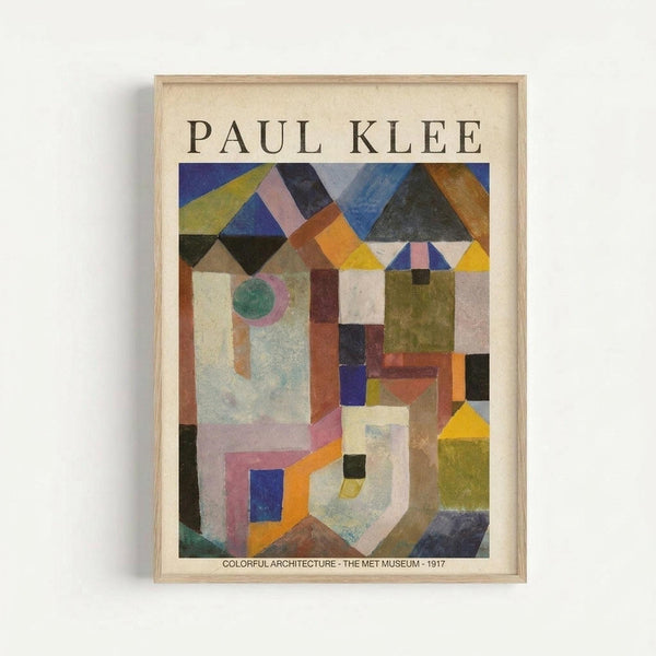 Framed art print of Paul Klee's abstract geometric composition featuring overlapping architectural forms in vibrant colors including blues, yellows, oranges, greens, and earth tones. The artwork shows angular shapes, triangular rooftops, rectangular buildings, and circular elements arranged in a cubist style. Text at bottom reads "COLORFUL ARCHITECTURE - THE MET MUSEUM - 1917". Light wood frame against white wall.