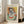 May include: Framed Picasso-style cubist portrait poster showing abstract figure with geometric face in blues, oranges, yellows and greens, leaning against beige armchair in bright living room with white walls and large windows