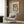 May include: Light gray upholstered armchair with geometric patterned pillow positioned beneath framed Picasso-style cubist portrait poster on wood-paneled wall. Artwork features abstract figure with curved forms in yellow, orange, blue and green colors. Modern brass floor lamp and dark side table with open book complete the contemporary room setting with natural lighting from window.