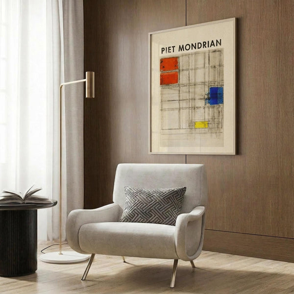 May include: Framed Piet Mondrian abstract composition study print with geometric grid and red, blue, and yellow color blocks, displayed on wood-paneled wall above beige upholstered chair with patterned throw pillow, alongside brass floor lamp and small side table with open book.