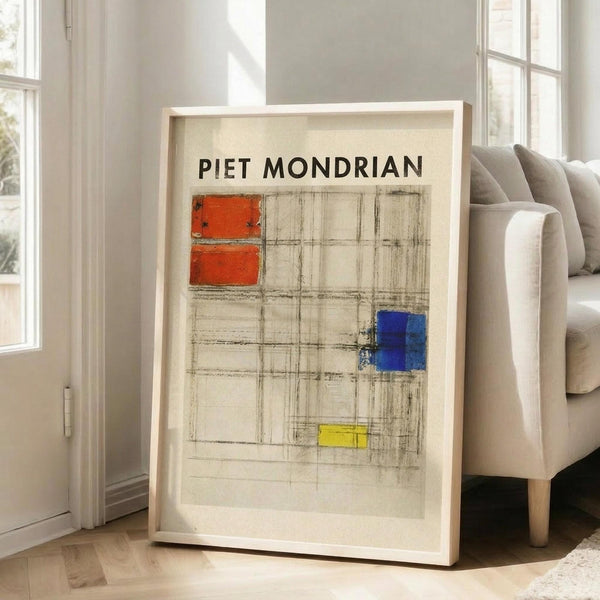 May include: Large framed poster print leaning against white wall next to beige upholstered chair in bright living room. The artwork shows Piet Mondrian's name in black text above an abstract geometric composition with red rectangles, blue square, yellow rectangle, and black grid lines on cream background. Natural sunlight streams through tall windows onto hardwood floors.
