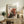 May include: Framed art print featuring abstract expressionist painting with bold black, red, and white paint splatters and drips displayed on rustic wooden sideboard in modern living room setting alongside fern plant, ceramic vase, and stacked books with warm natural lighting and neutral beige walls.