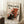 May include: Abstract art poster with black, red, and white paint splatters in Pollock's signature drip style, displayed in thin wooden frame leaning against white wall. Coffee cup on wooden block sits nearby on textured cream rug, with soft natural lighting creating gentle shadows.