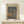 May include: Framed Paul Klee art poster featuring abstract organic shapes in blue and brown tones, displayed on light wood console table beside small white wrapped gift with twine and greenery sprig against cream wall