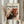 May include: Person in beige ruffled sleeves holding framed abstract art poster with black paint splatters and red drips on cream background, featuring "POLLOCK" text and dates "1912-1956." Light wood frame against white curtained window with dried pampas grass visible to left side.