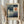 May include: Hands holding a framed vintage exhibition poster featuring Paul Klee's geometric abstract artwork with blue rectangular blocks, white crescent moon, and orange circle with black stem. Light wood frame against neutral curtain backdrop with dried wheat stems visible on left side.