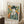 May include: Framed Picasso-style portrait print leaning against white wall in cozy room setting. Artwork shows figure in dark hat and blue clothing with white collar against colorful geometric background. Light wood frame, positioned on textured cream rug next to wooden side table with coffee cup and beige chair arm visible.
