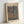May include: Framed museum poster featuring Paul Klee's abstract artwork with organic blue and brown shapes resembling cellular or stone-like patterns against an earthy background. The print displays museum text at bottom and sits in a light wood frame, leaning against a white wall on a light surface.
