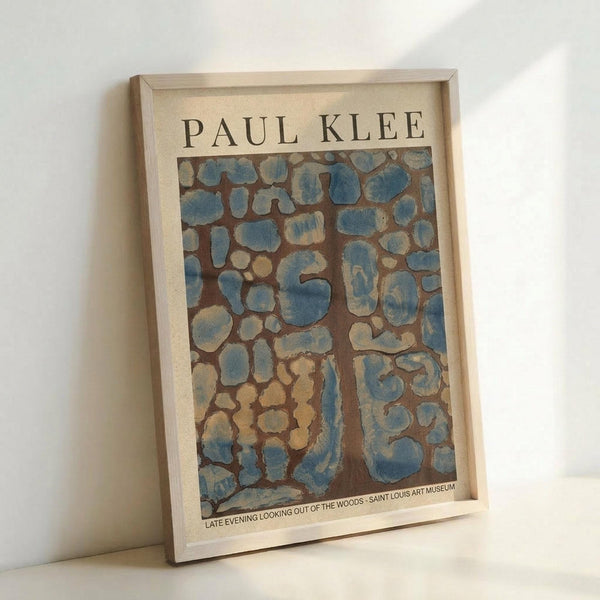 May include: Framed museum poster featuring Paul Klee's abstract artwork with organic blue and brown shapes resembling cellular or stone-like patterns against an earthy background. The print displays museum text at bottom and sits in a light wood frame, leaning against a white wall on a light surface.