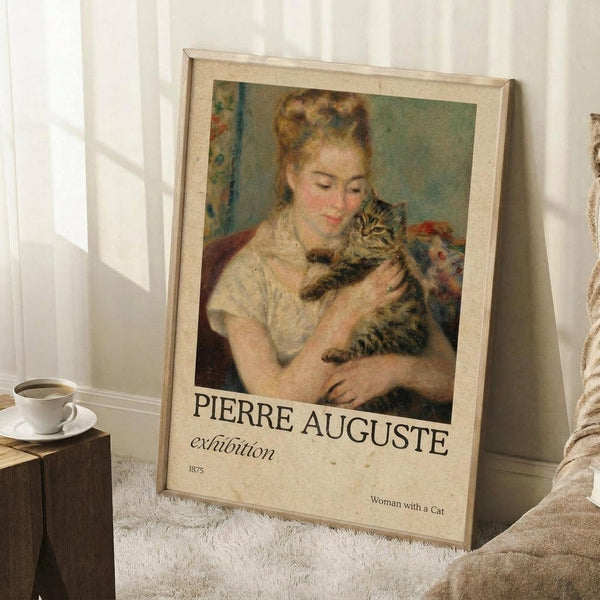 May include: Framed exhibition poster featuring Renoir's 1875 painting of a woman in white dress holding a tabby cat, with cream matting and light wood frame. Poster leans against white wall on textured white rug next to wooden side table with coffee cup and saucer. Soft natural lighting creates gentle shadows across the scene.