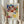 May include: Person in cream blouse holding framed Paul Klee exhibition poster featuring abstract watercolor composition of overlapping geometric shapes in blues, reds, yellows, greens, and purples. Light wooden frame against white curtained window with dried wheat stalks visible on left side.