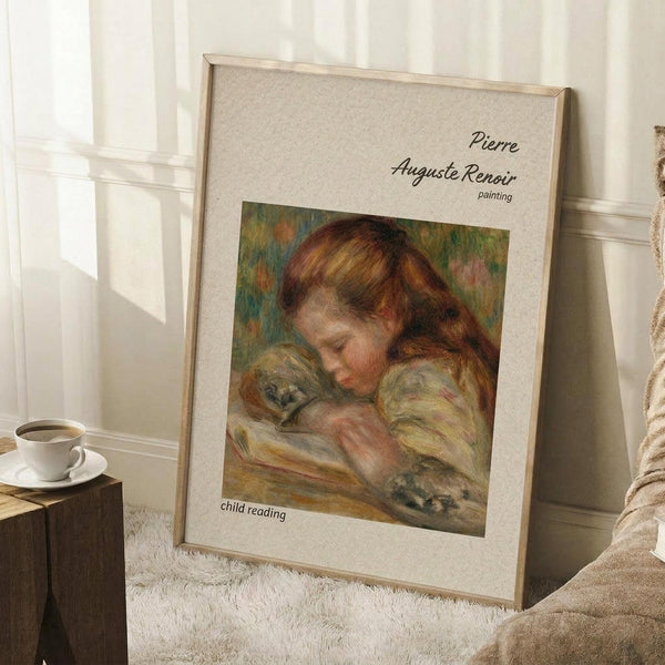 May include: Framed poster print of a Renoir painting showing a young child with reddish-brown hair reading a book, rendered in soft impressionist brushstrokes with warm earth tones. The beige matted frame leans against white wainscoting beside a wooden side table with coffee cup, on a textured cream rug next to a beige upholstered chair in natural lighting.