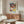 May include: Colorful Paul Klee abstract artwork poster displayed above wooden credenza in modern living room. The framed print features geometric squares and rectangles in vibrant blues, reds, yellows, and greens with varied textures and patterns. White curved chair and glass coffee table complete the minimalist Scandinavian-style interior with beige walls and natural lighting.