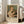 May include: Framed exhibition poster featuring Pierre Auguste Renoir's 1875 painting of a blonde woman in white clothing tenderly holding a striped tabby cat. The vintage-style poster has cream matting and light wood frame, leaning against white walls near large windows in a bright living room with beige sofa and pillows visible.