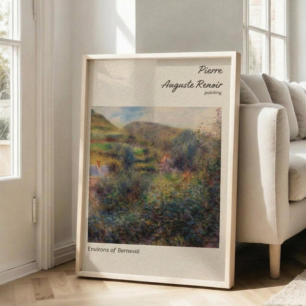 May include: Framed Renoir landscape painting print leaning against beige armchair in bright living room with white walls and windows. The artwork shows rolling hills with lush vegetation in impressionist style using greens, blues, and earth tones. Natural wood frame with cream matting displays the pastoral countryside scene with soft, dreamy brushwork typical of Renoir's plein air landscapes.