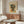 May include: Colorful geometric Picasso-style face poster with angular features in blues, greens, oranges and yellows, displayed above a mid-century modern walnut credenza. Room features white curved chair, glass oval coffee table, modern brass floor lamp, and neutral walls with natural lighting.
