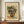 May include: Framed vintage-style cubist portrait poster featuring an abstract face with geometric shapes in orange, blue, green, and yellow tones, displayed on a wooden credenza alongside a white ceramic vase and stacked books in a room with cream walls and white trim molding.