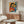 May include: Modern living room with wooden credenza displaying framed Picasso-style poster featuring two embracing women in cubist style with vibrant orange, blue, and red colors. White upholstered chair, glass coffee table, and minimalist brass floor lamp complete the contemporary interior setting.