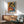 May include: Framed Picasso-style poster featuring two women in an abstract cubist composition with warm orange, blue, and red tones, displayed above a wooden sideboard with white ceramic lamp in a modern living room setting with mint green mid-century chair and natural lighting creating geometric shadows on white wall