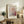 May include: Framed Paul Klee exhibition poster in light wood frame leaning against white wall on rustic wooden sideboard. Abstract artwork features pink and orange spiral flower design with dotted pattern background. Styled with fern plant, leather chair, stacked books, and ceramic vase in warm, minimalist living room setting.