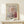 May include: Framed poster with abstract artwork featuring dotted patterns in pink, orange, and blue circles on white background with geometric lines, displayed on light wooden surface next to small white wrapped gift with greenery sprig against cream wall