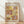 May include: A framed Paul Klee exhibition poster displayed against a white wall on light wood flooring. The artwork features abstract geometric shapes in warm earth tones of yellow, pink, brown, and cream with delicate line drawings of plants, figures, and botanical elements. The poster has "PAUL KLEE" at the top and museum text at the bottom, all within a thin wooden frame. Soft natural lighting creates diagonal shadows across the white textured wall.