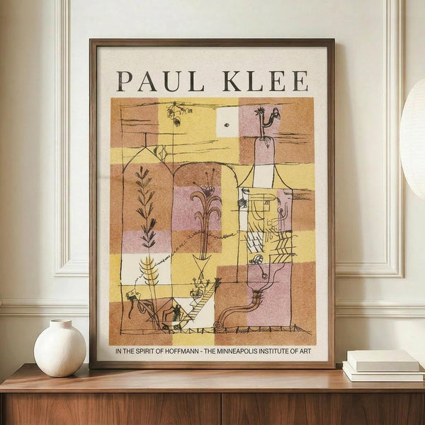 May include: Framed Paul Klee exhibition poster featuring abstract geometric artwork in warm yellows, pinks, and browns with whimsical line drawings of plants and figures. The vintage-style print sits on a wooden sideboard next to a cream ceramic vase and stacked books in a bright room with white paneled walls.