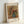 May include: Framed art print featuring Pierre Auguste Renoir's impressionist painting of pink and peach flowers in a blue-green ceramic pitcher. The artwork shows soft, loose brushstrokes with warm golden background tones. White matting surrounds the image with "VASE OF FLOWERS" printed at top and "PIERRE AUGUSTE RENOIR" at bottom. Light wood frame rests against white wall on white surface, casting subtle shadow.