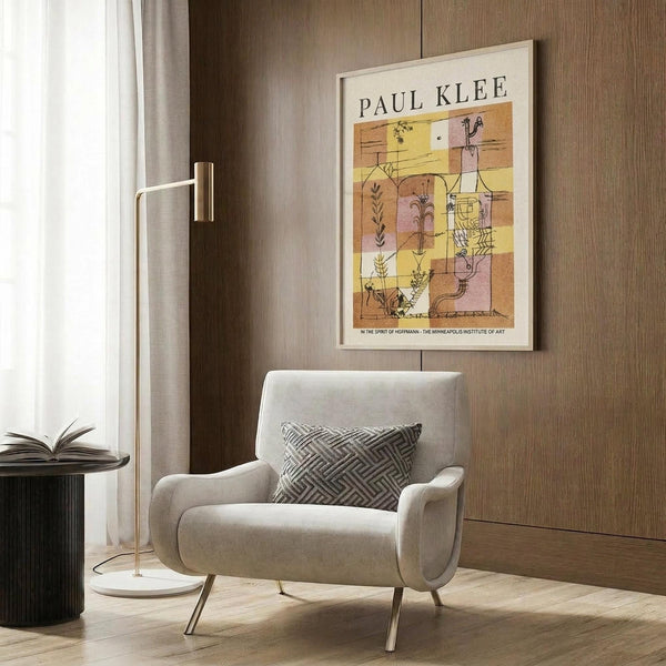 May include: Paul Klee art print in light wood frame hanging on textured brown wood paneling above a cream upholstered armchair with geometric patterned pillow. Abstract artwork features warm yellow, orange and pink rectangular sections with delicate botanical line drawings. Modern brass floor lamp and black side table with open book complete the cozy reading nook scene with natural lighting from nearby window.
